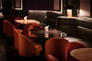A restaurant interior with red chairs, tables, artwork, and candles creating a warm and inviting atmosphere