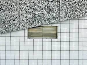 A minimalist interior space with a checkered tiled wall featuring a built-in metal box, creating a geometric and modern look