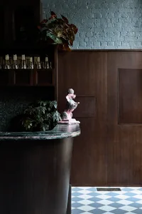 Dark bar area with a marble countertop, a pink statue, and bottles adding to the sophisticated ambiance