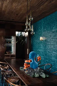Warm and inviting dining area with a wooden table, chairs, wine glasses, and fresh fruits, set against a brick-patterned wall