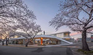 A modern building with a large glass wall, balcony, and staircase, surrounded by potted plants and featuring a stylish and functional design
