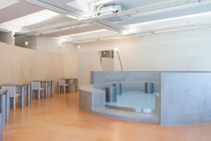 A modern restaurant with a circular dining area surrounded by multiple dining tables and chairs, featuring a combination of wood and metal elements in a dimly lit space