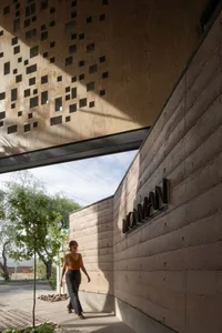 A woman walks through a calm and serene indoor space with a stone wall and a natural backdrop of trees