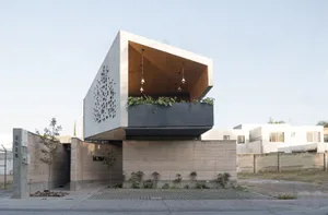 A modern building with a concrete facade, featuring a large overhang and potted plants around the structure, conveying a sense of urban design and contemporary architecture