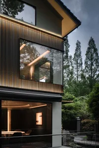 A modern house with large windows, glass, and wood elements, surrounded by trees and natural light