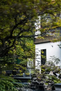 A serene Asian-style house with a white exterior, surrounded by trees and greenery, featuring a large window and a blend of traditional and modern architectural styles