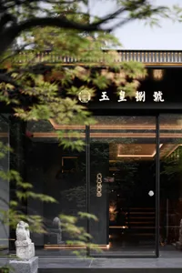 A traditional Asian building with a black doorway leading to a well-lit hallway featuring two statues on display