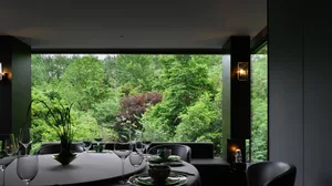 Dining area with a large window offering a view of trees, elegant table setting with wine glasses, bowls, and cups, and comfortable seating