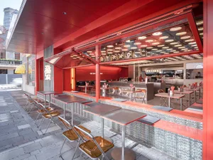 A modern Asian restaurant interior with a red accent wall, natural light, and dining tables and chairs