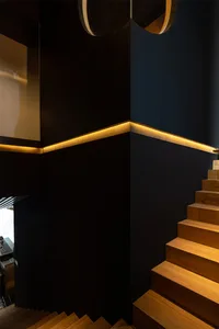 A black staircase with a wooden railing leads to another level of a building