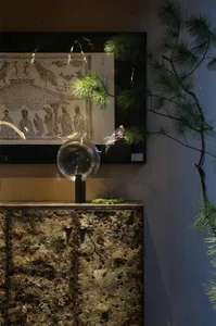 A living area with a stone table, glass bowl, and several potted plants, featuring three decorative figures