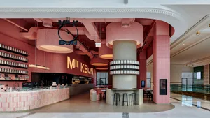 Inviting restaurant interior with a pink and white color scheme, featuring a bar, dining table, and various seating options, with bottles and a welcoming atmosphere