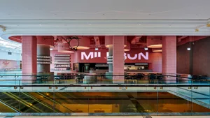 A modern restaurant with pink walls, a glass ceiling, and natural light, featuring multiple tables and chairs, and several people enjoying their meals