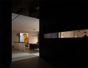 Dark dining room with a black doorway, chairs around a dining table, and a kitchen area with a sink and refrigerator