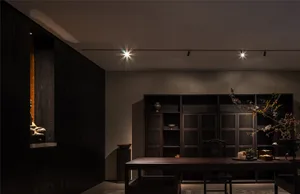 Cozy living space with wooden floors and walls, a dining table, chairs, and decorative vases, bathed in warm lighting