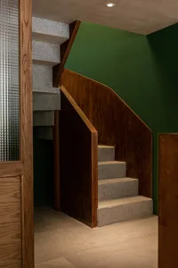A wooden staircase with brown treads and a door at the bottom, leading to a warm and inviting home environment
