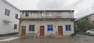 Aged building with a weathered concrete facade, featuring two doors and two windows, with a neglected appearance