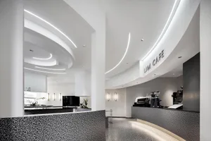 Modern restaurant with a circular dining area, white walls, grey flooring, and potted plants, featuring a bar and multiple dining tables