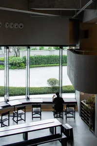Calm and inviting living-dining space with natural light, wood, and glass, featuring a man sitting at a desk in front of a window