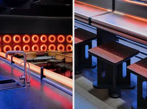 Modern restaurant interior with dining tables, chairs, a bar area, and red accents