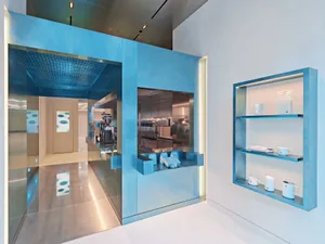 Modern kitchen with bright blue walls, large window, appliances, and scattered cups, featuring a clean and contemporary design