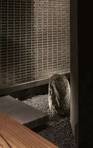 A minimalist interior space with a rock placed on gravel in front of a glass wall, creating a modern and unique focal point