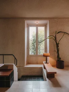 Modern bathroom with a sink, toilet, and shower area, featuring concrete walls, a large window, and a potted plant