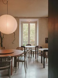 A restaurant dining area with white tables, potted plants, and chairs arranged around them, creating an inviting and comfortable atmosphere