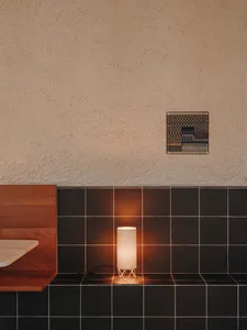 A bathroom with a tiled wall and a wooden countertop, lit by two lights, creating a clean and well-lit environment