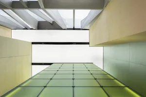 A modern interior space with a large green-tinted glass wall extending upwards, creating a sense of openness and spaciousness