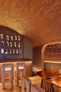 A modern restaurant interior with a brick wall, wooden tables, and a warm ambiance, featuring three chairs and rustic walls