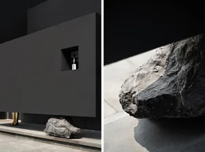 Dark modern house with a floor plan showing a kitchen area with a sink and dining table, and an architectural scene with large concrete rocks in front of a black wall