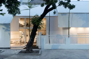 A modern outdoor space with a white metal building and a large tree in front, featuring several chairs and two dining tables