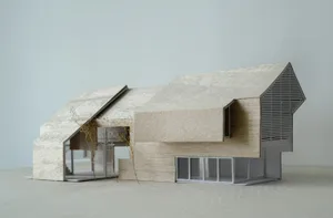 Architectural model of a wooden house with a large window and smaller window, two doors, and a warm inviting atmosphere