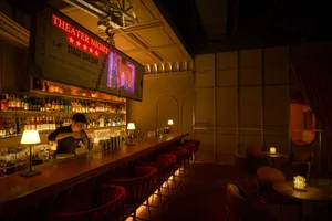 A cozy bar area with red chairs, a counter, and bottles, cups, and wine glasses, set in a restaurant setting