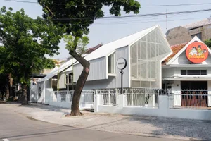 A modern house with a white facade, a large glass wall, and a balcony, surrounded by two trees