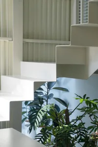 A modern staircase with white concrete steps, surrounded by potted plants and a decorative vase, in a residential living area