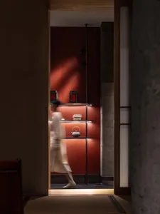 A woman walks through a warm and inviting orange room with a display of vases on the wall, creating an artistic atmosphere