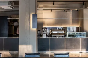 Industrial kitchen with espresso machines, modern appliances, and scattered cups, suggesting a functional and modern design