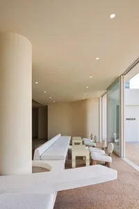 Modern open space with a glass wall, a long bench, and multiple chairs, surrounded by white walls and furniture, with natural light filling the room