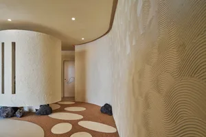 A hallway with a curved wall and decorative elements, including a potted plant, vases, and bowls, with chairs scattered throughout