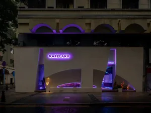 A modern building with purple lights and a large archway, surrounded by potted plants and greenery