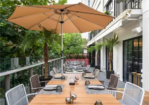 A well-lit outdoor dining area with a wooden table surrounded by chairs and umbrellas, creating a relaxed atmosphere for guests to enjoy their meals