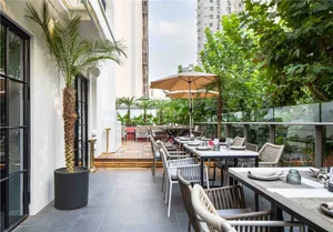 Outdoor dining space with concrete flooring, wooden tables and chairs, and umbrellas providing shade, surrounded by potted plants