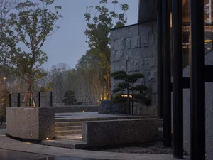 A modern house at night with a large stone building and black doorway, surrounded by trees and artificial lighting