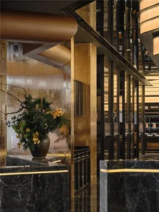 A hotel lobby with a large vase of yellow flowers on a table, surrounded by potted plants, in a well-lit space