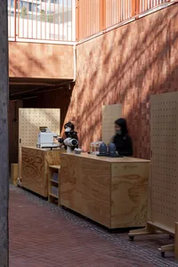 A casual cafe interior with a counter and seating area, featuring a woman wearing a mask and serving drinks and food