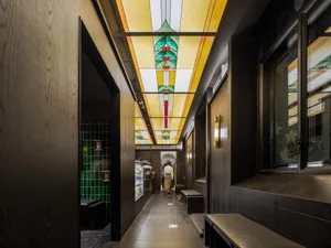 A modern cafe with green and brown tile walls, benches, and a hallway separating two dining areas