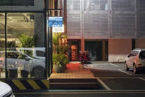 A building exterior at night with two parked cars and potted plants, illuminated against a dark background