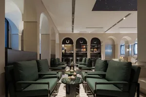 Cozy living space with green couches, chairs, a marble table, and a bar area with multiple bottles